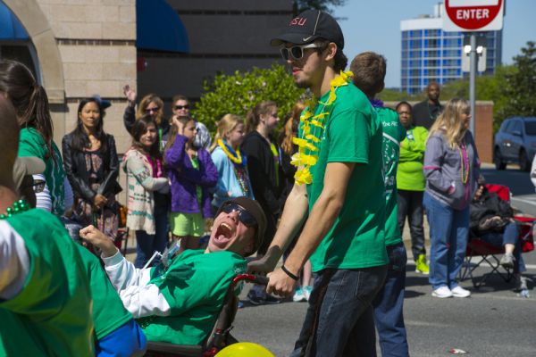 Man pushing a man in a wheelchair in a parade.